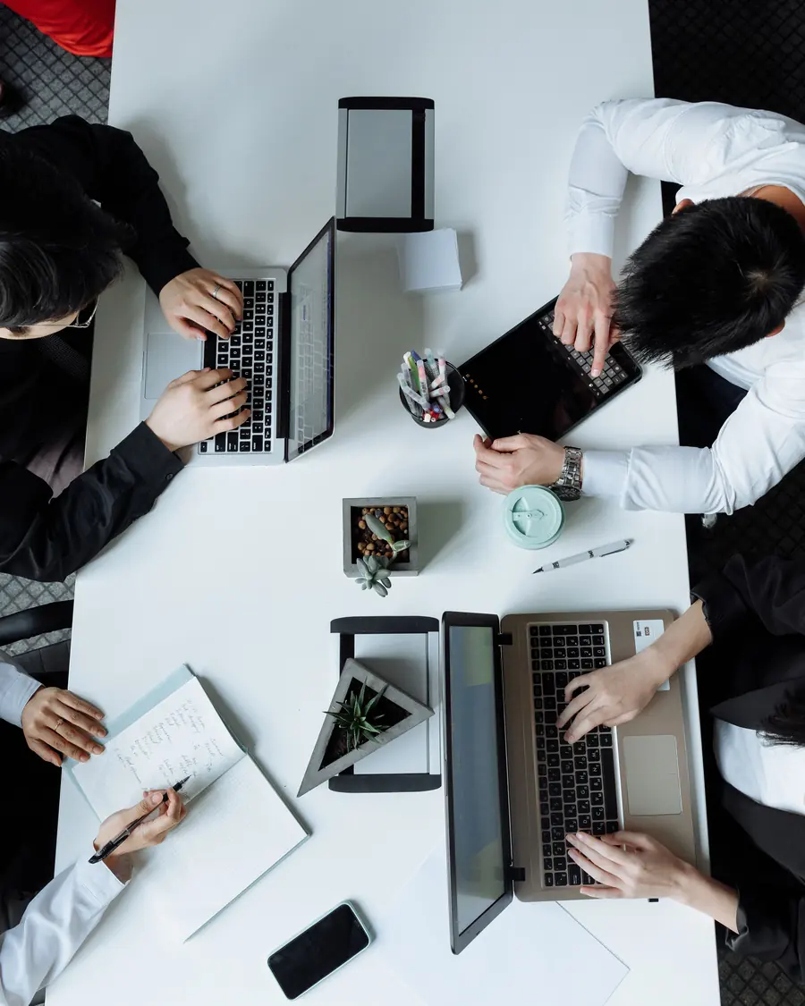 Team collaborating over laptops and notebooks at a shared table, seen from above